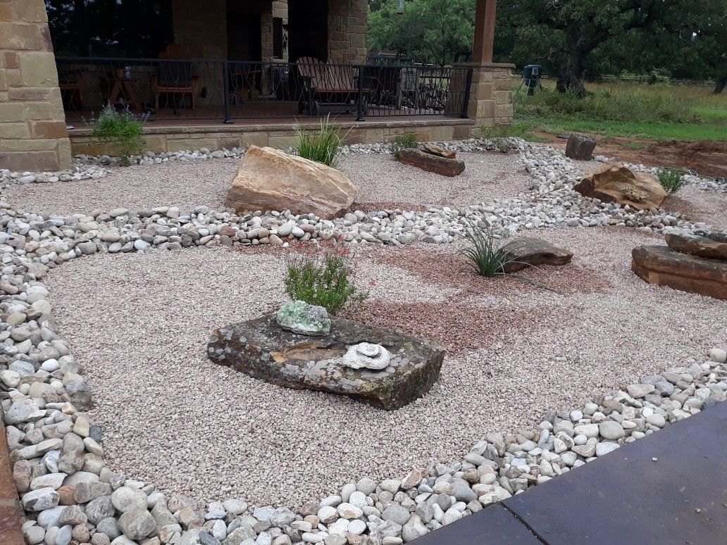 A garden filled with rocks and plants in front of a house.