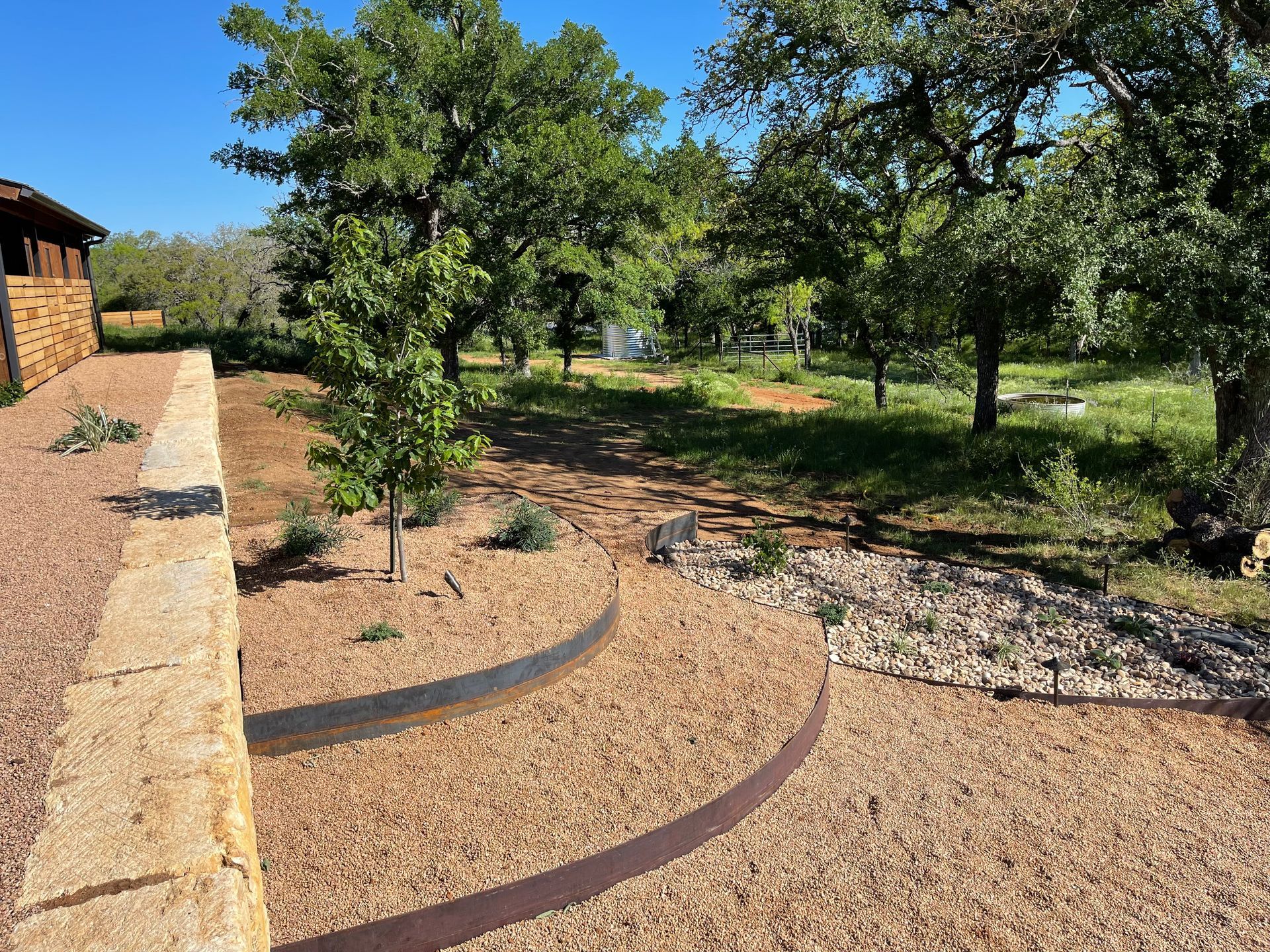 A stone wall is surrounded by gravel and trees.