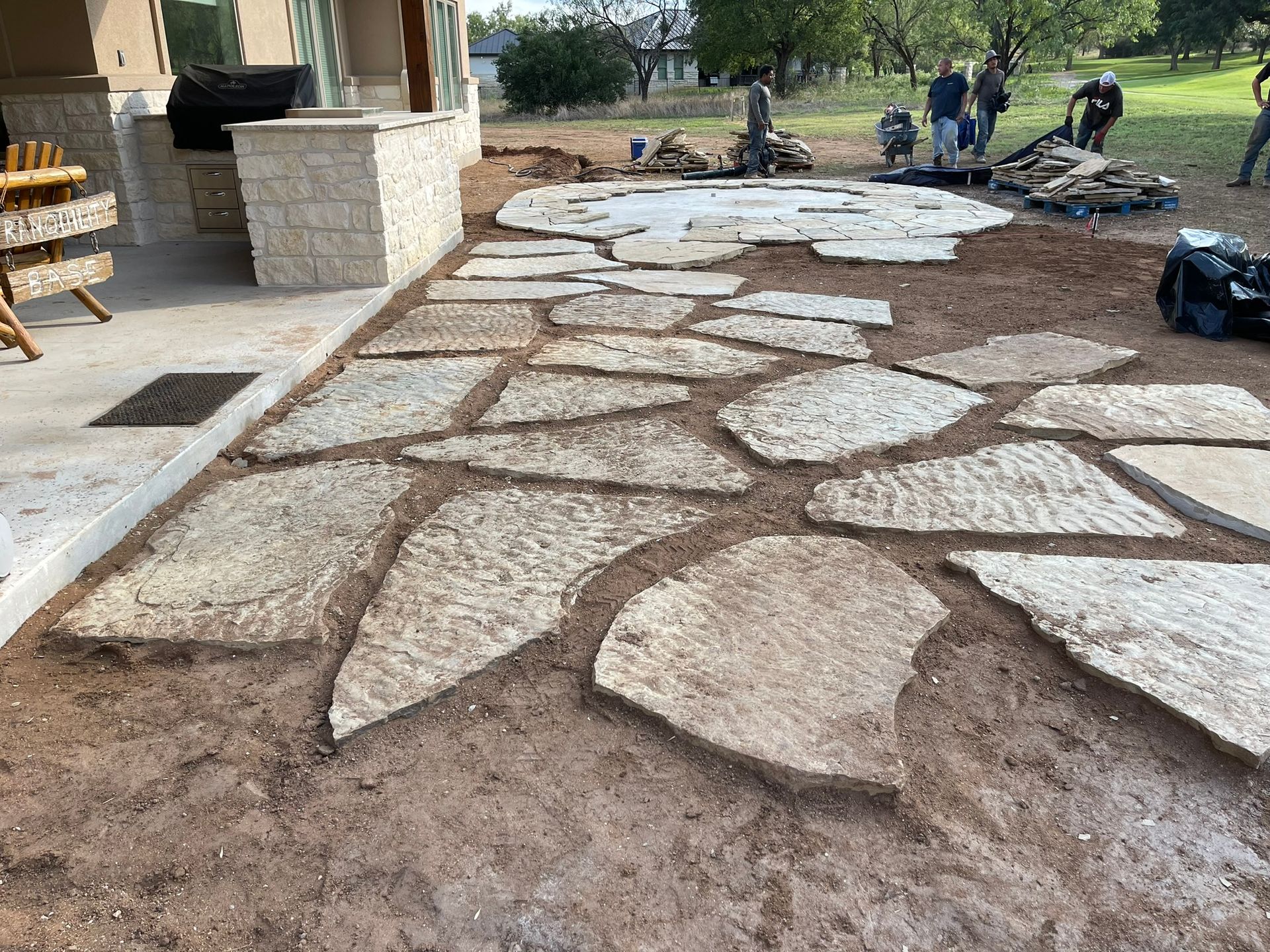 A stone walkway is being built in the backyard of a house.
