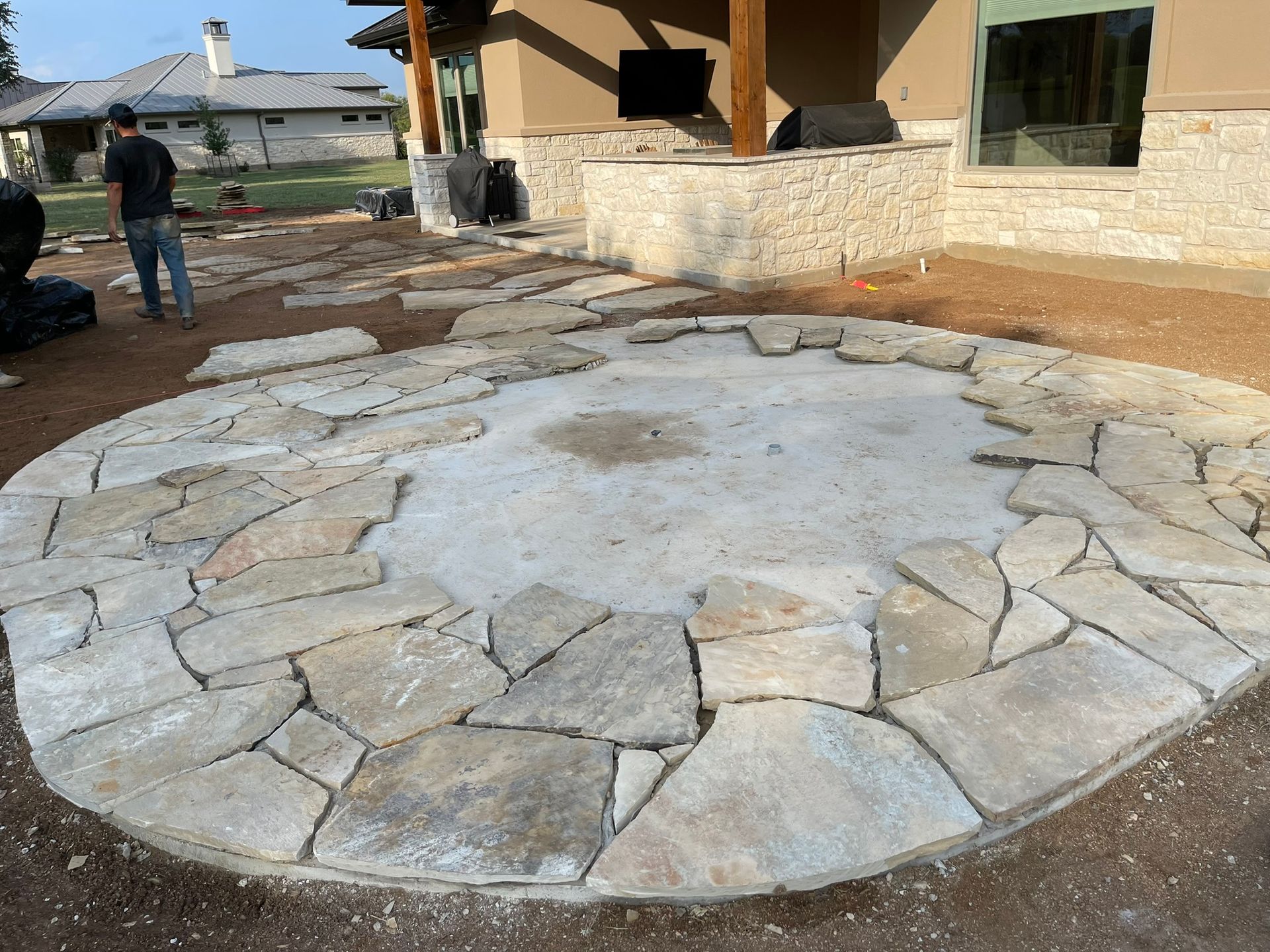A man is standing in a circle of rocks in front of a house.