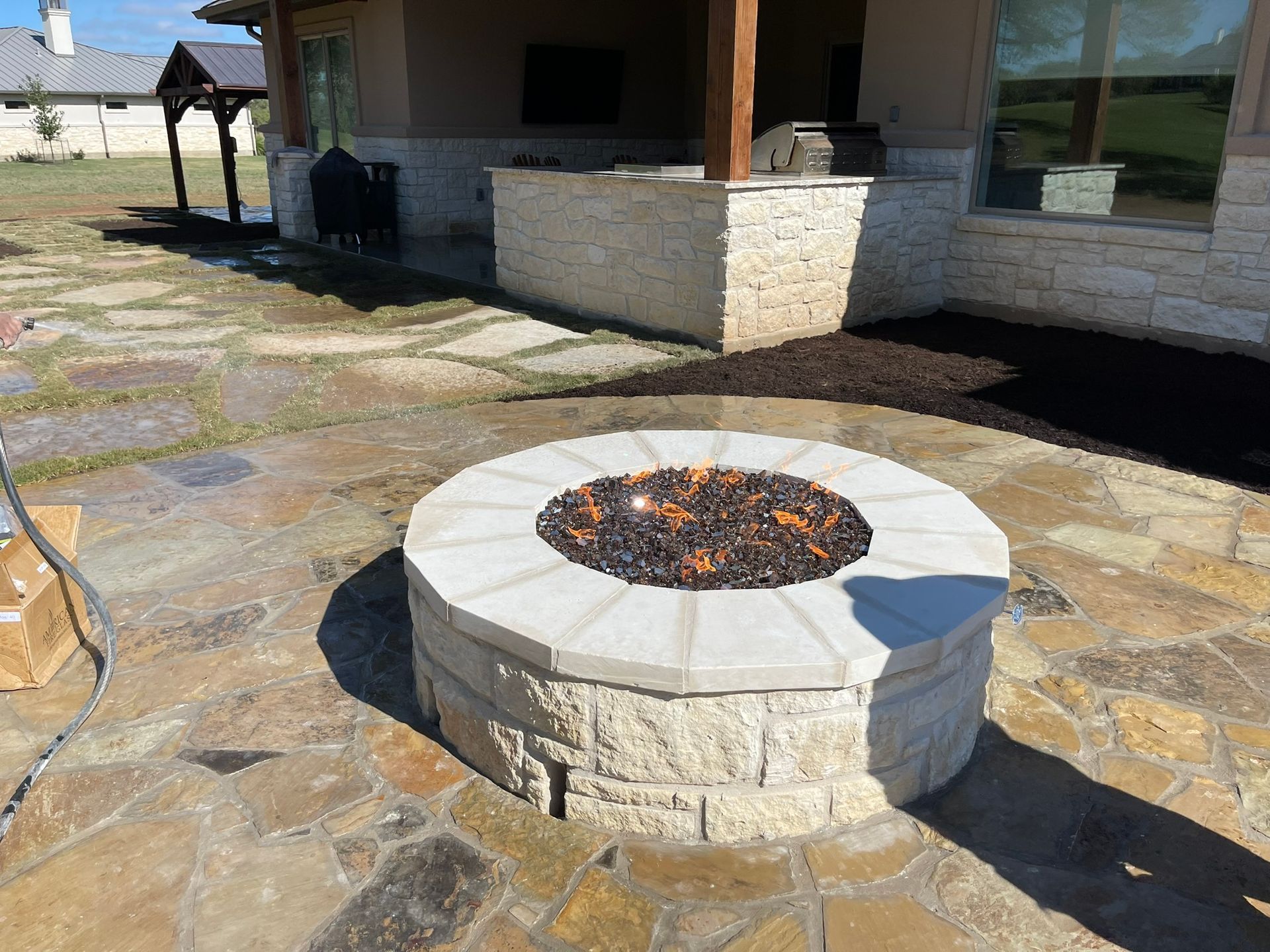 A fire pit is sitting on a stone patio in front of a house.
