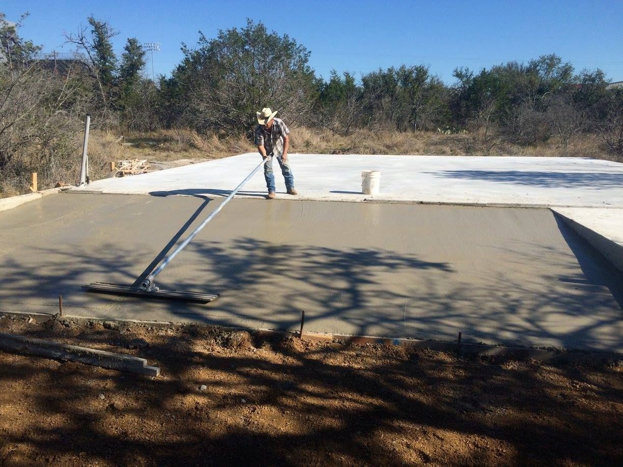 A man in a cowboy hat is using a broom on a concrete surface.