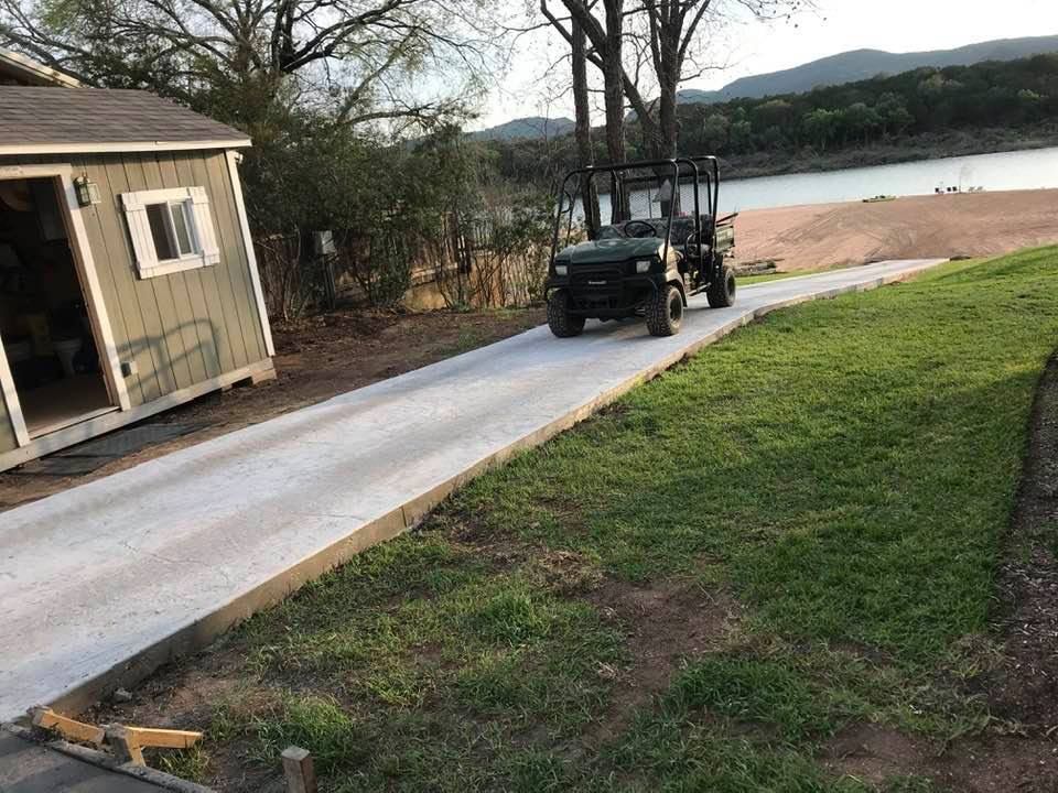 A golf cart is driving down a concrete driveway next to a shed.