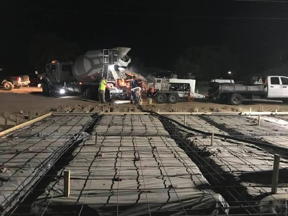 A group of construction workers are working on a concrete floor at night.
