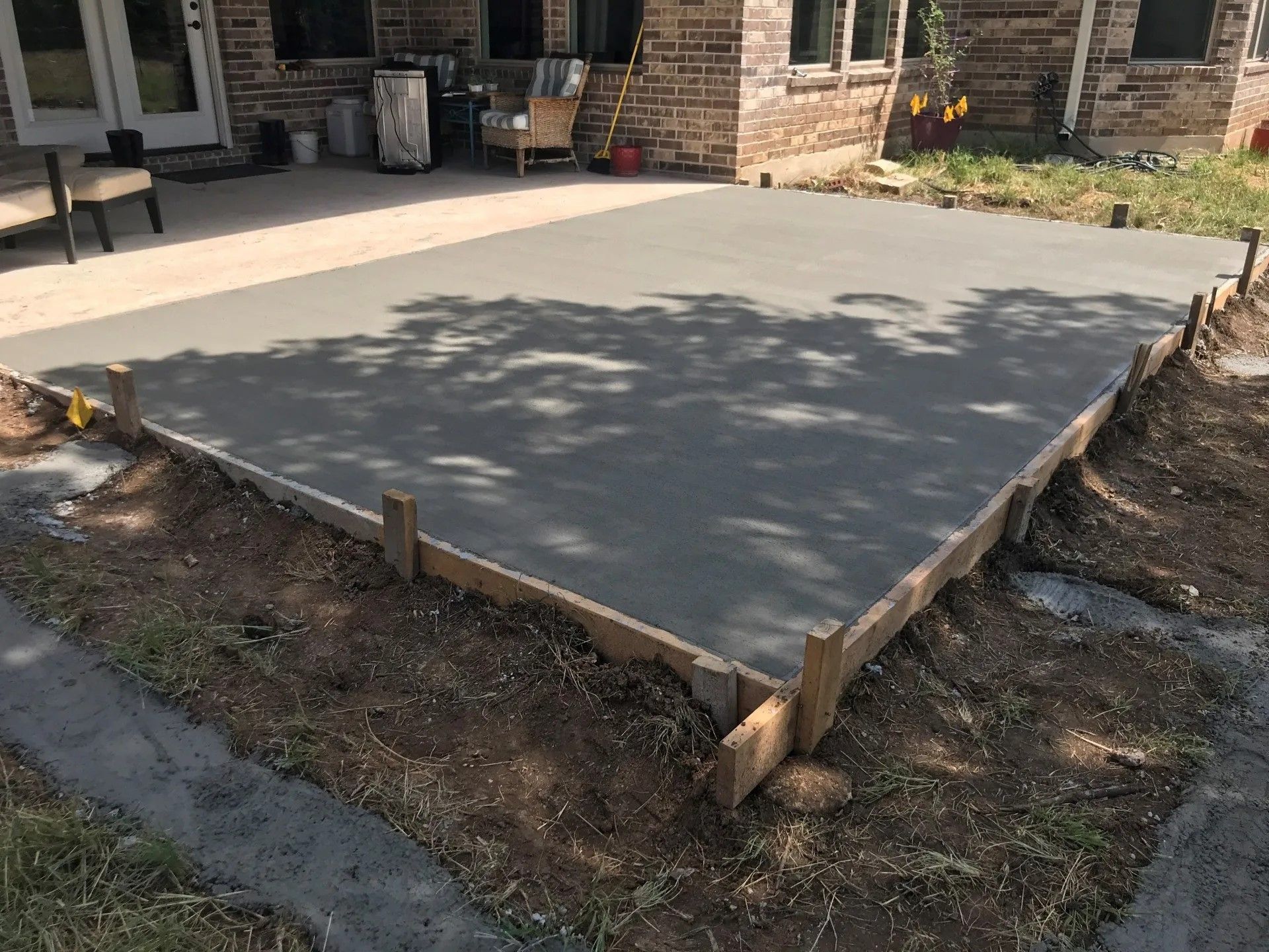 A concrete patio is being built in front of a brick house.