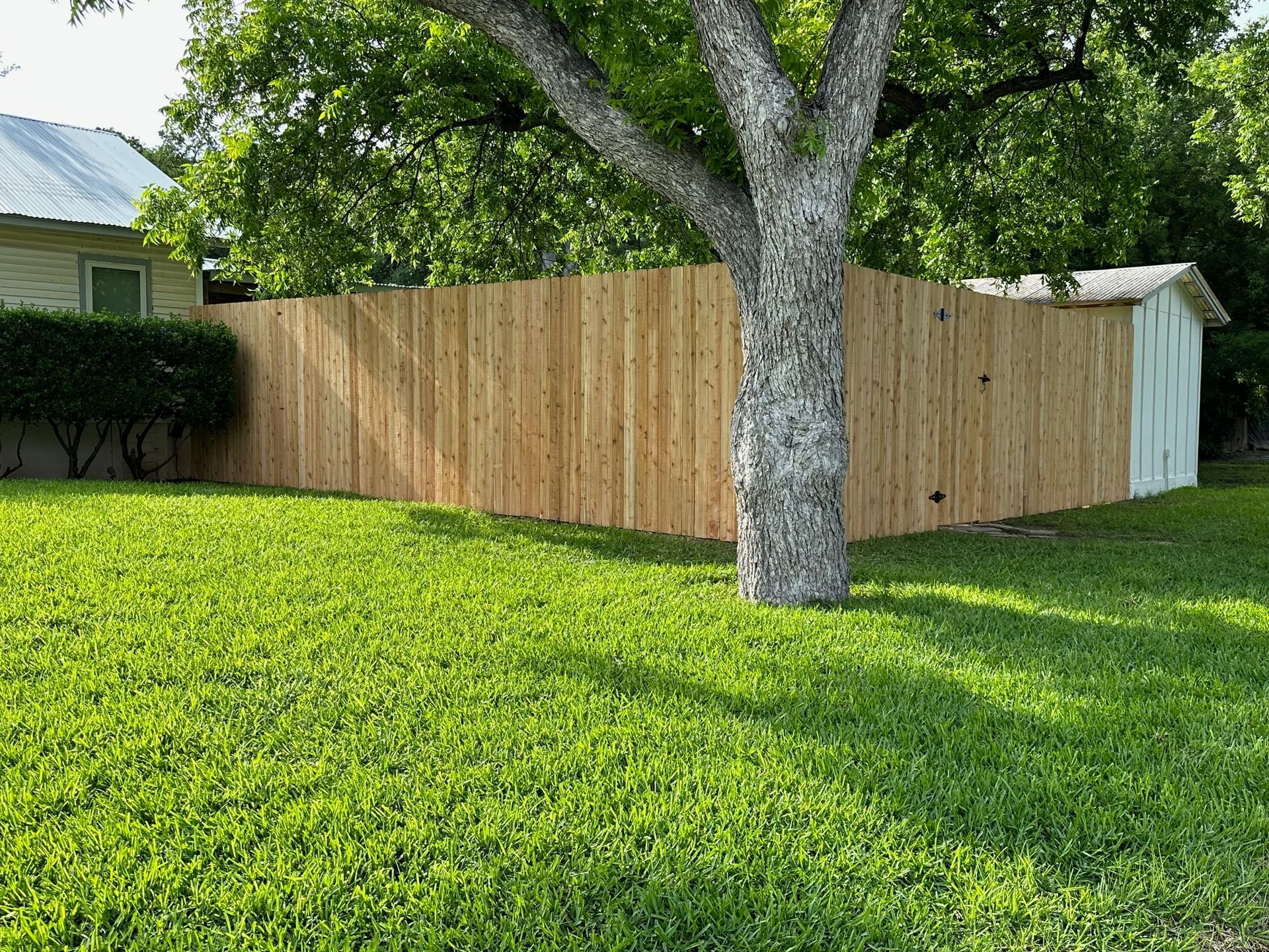 A wooden fence is in the middle of a lush green yard.