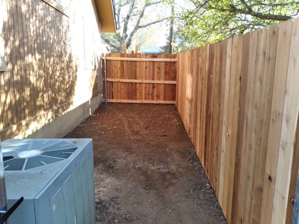 A wooden fence surrounds a dirt area next to a house.
