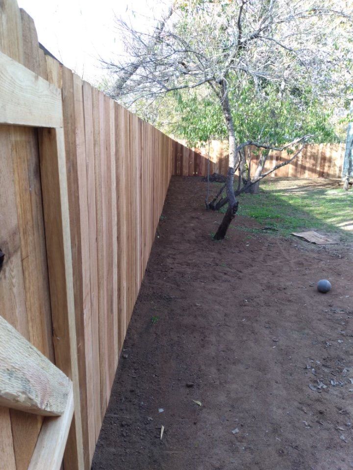 A wooden fence is surrounded by dirt and trees in a backyard.