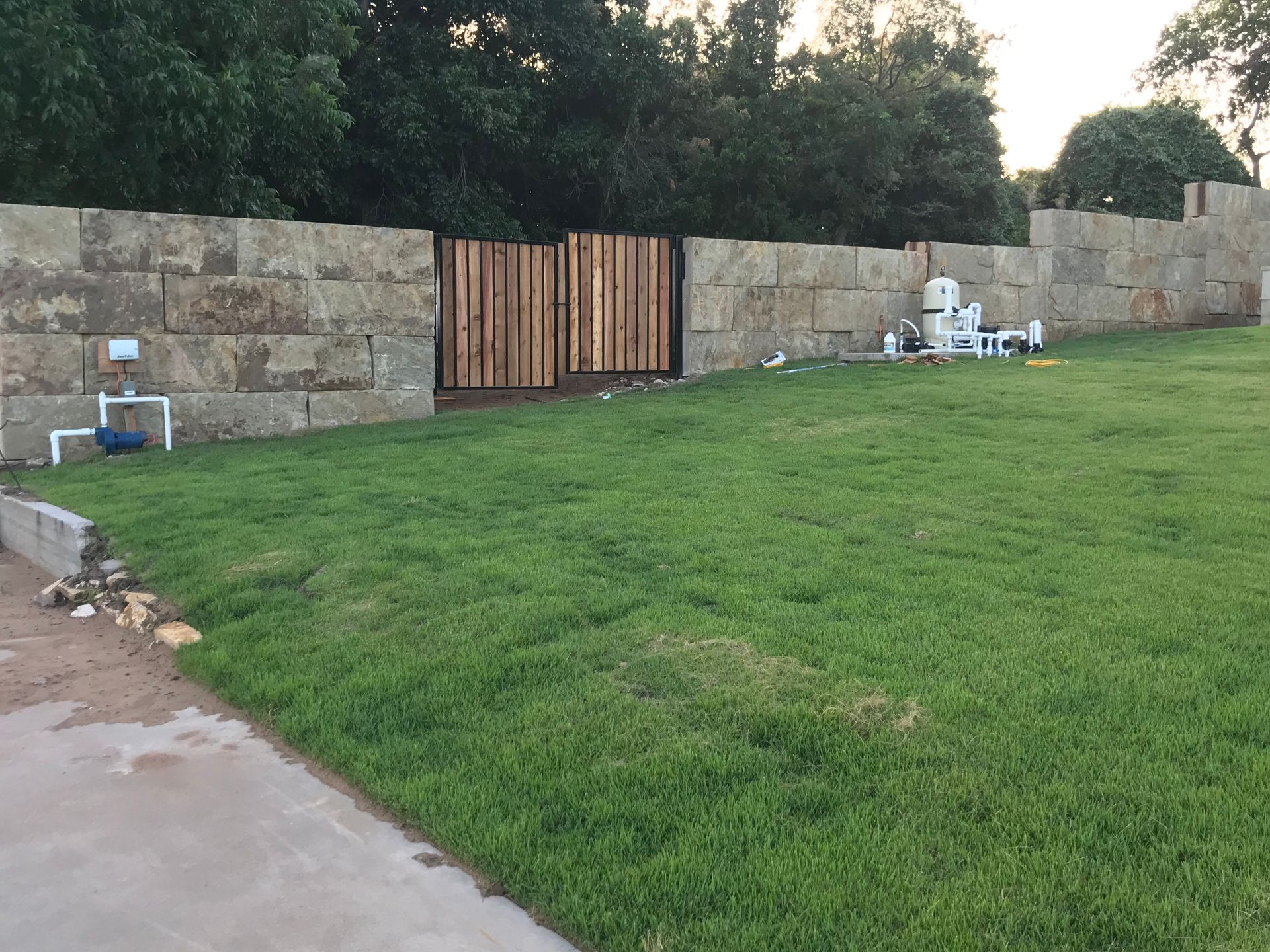 A large lawn with a stone wall and a wooden gate