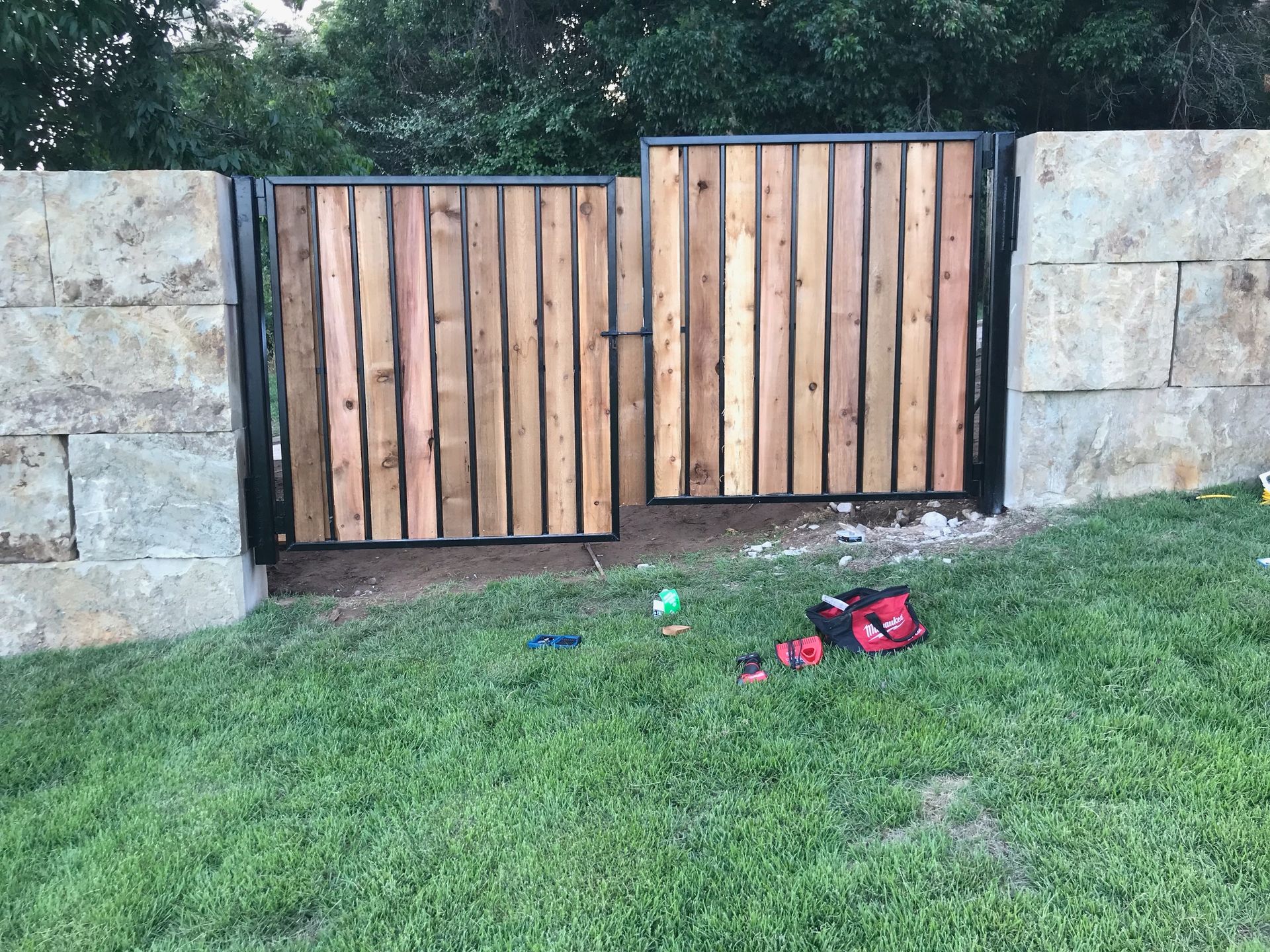 A wooden gate is sitting in the grass next to a stone wall.