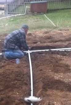 A man is kneeling down in the dirt working on a pipe.