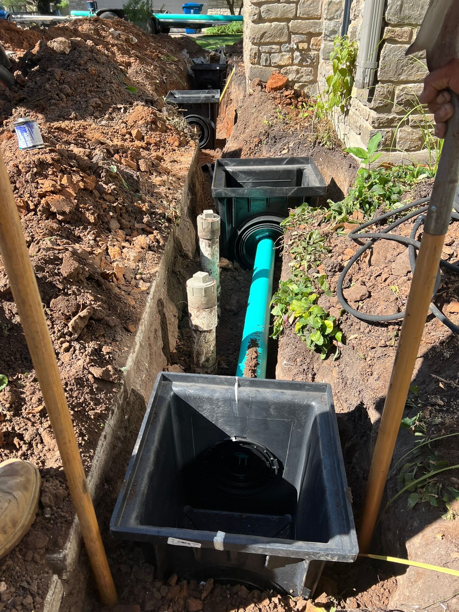 A green pipe is being installed in the ground next to a brick wall.