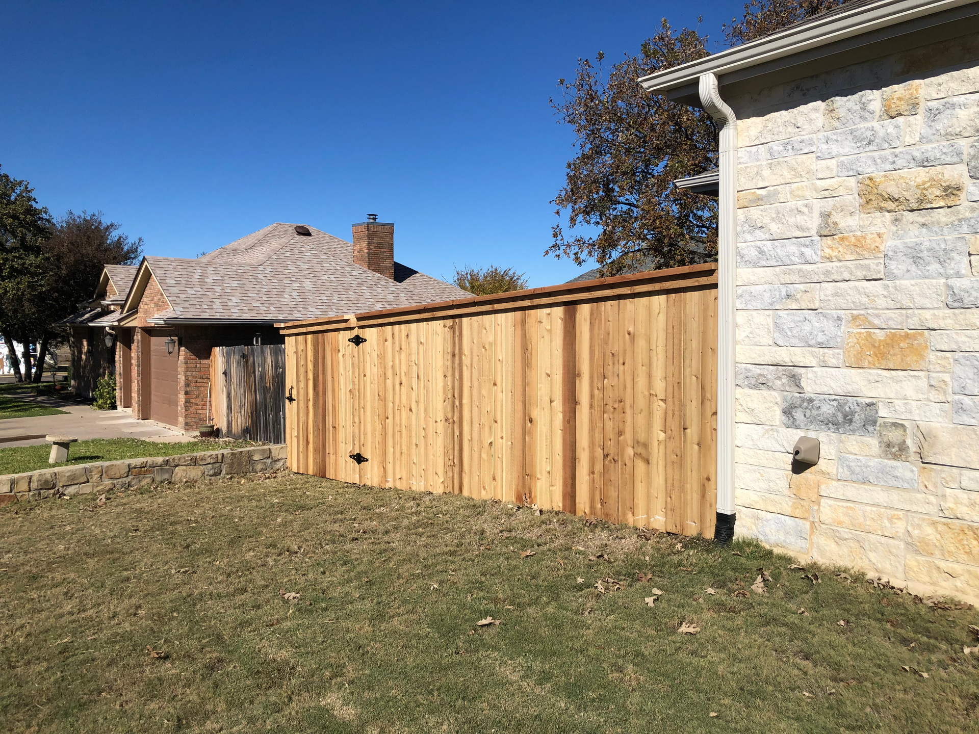 A wooden fence is sitting next to a stone wall in front of a house.