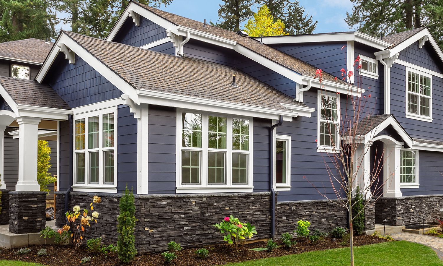 Blue two-story house with white trim, dark stone accents, and multiple windows; green lawn.