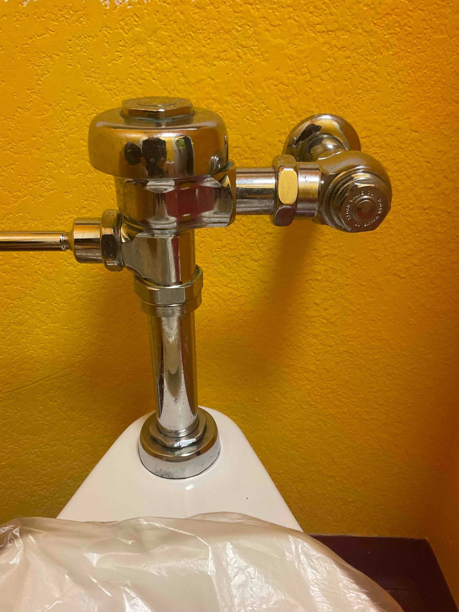 Chrome flush valve mounted on a white urinal against a yellow wall