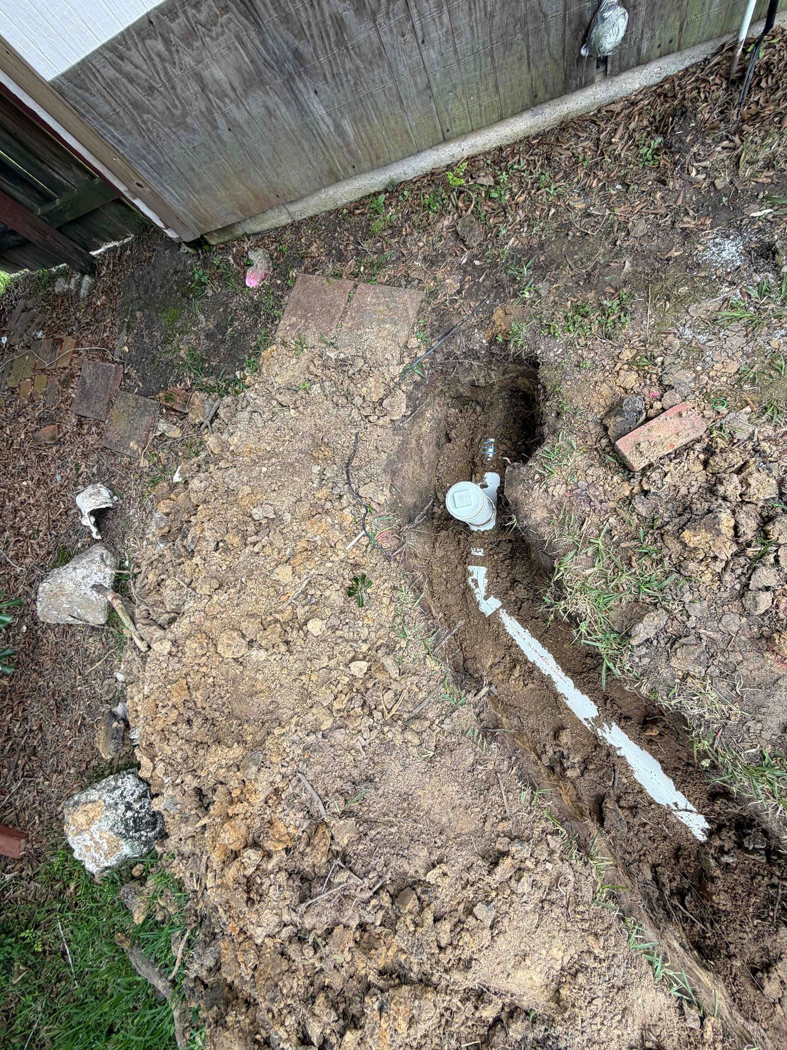 Damaged dirt path beside a wooden fence, with a small hole and scattered debris
