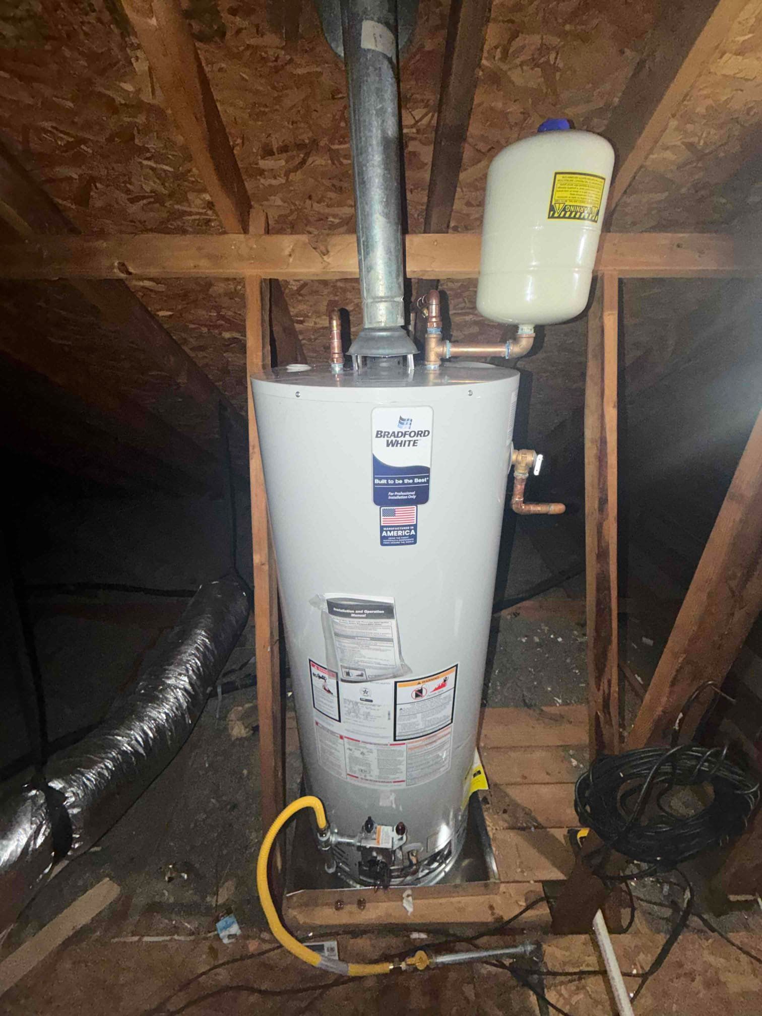 Water heater in an attic with exposed wooden rafters and ductwork.