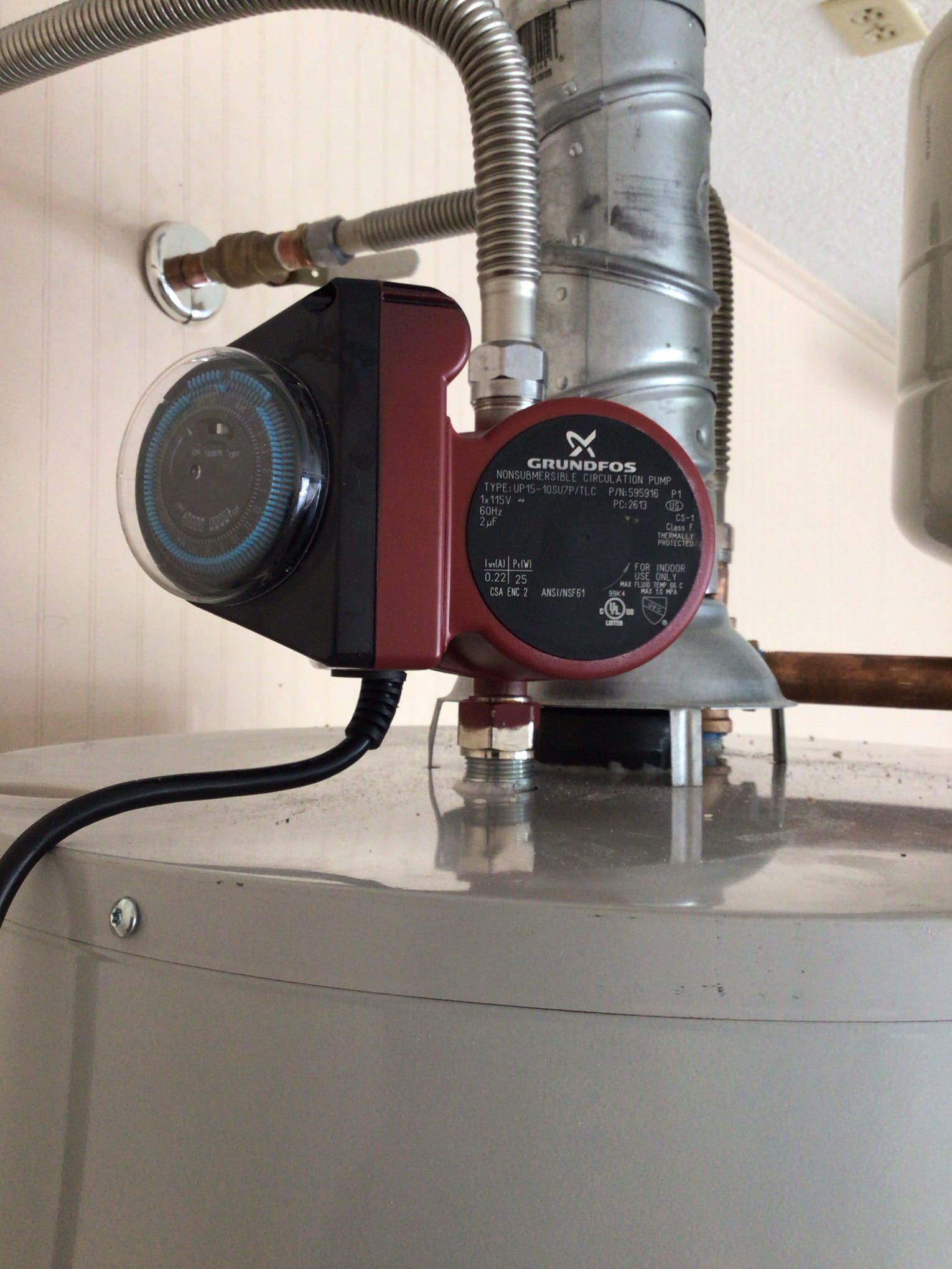 Red circulation pump mounted on a metal water heater with silver pipes and a pressure gauge.