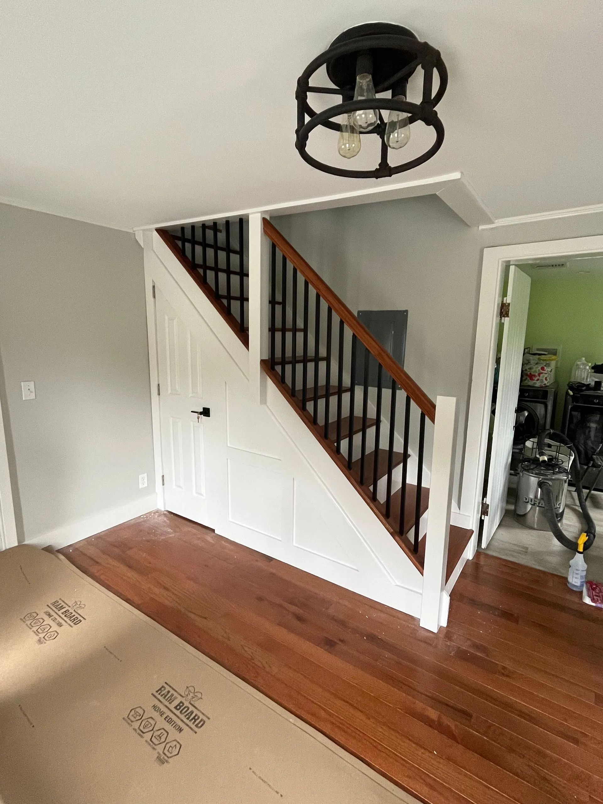 Staircase with black metal railing, wooden steps, and a black ceiling light.