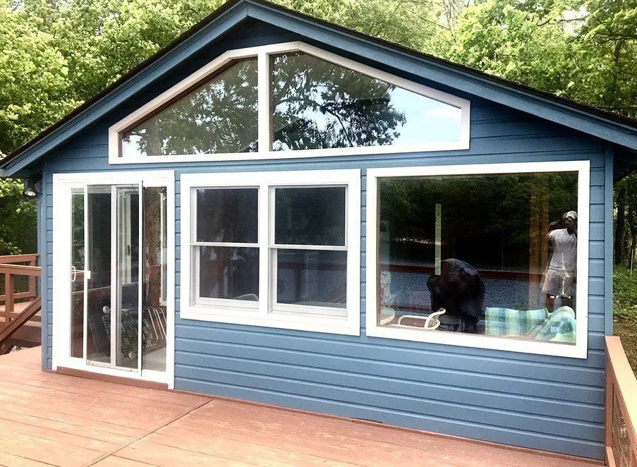 Blue cabin with large windows and a sliding door, on a wooden deck.