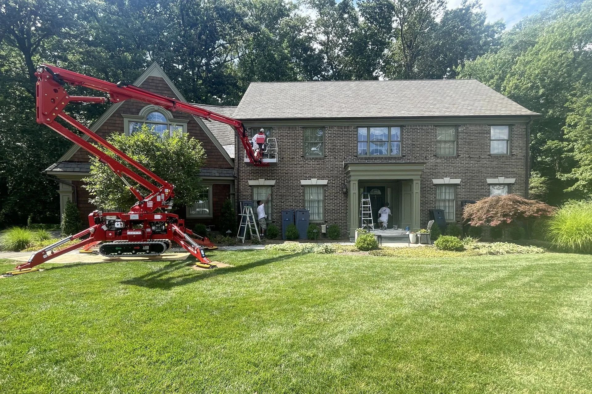 Red lift in front of a house, possibly for exterior work. Green grass and trees are in the background.