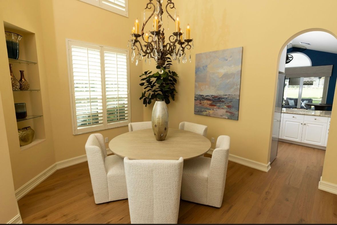 Dining room with round table, four white chairs, chandelier, artwork, and arched doorway to kitchen.