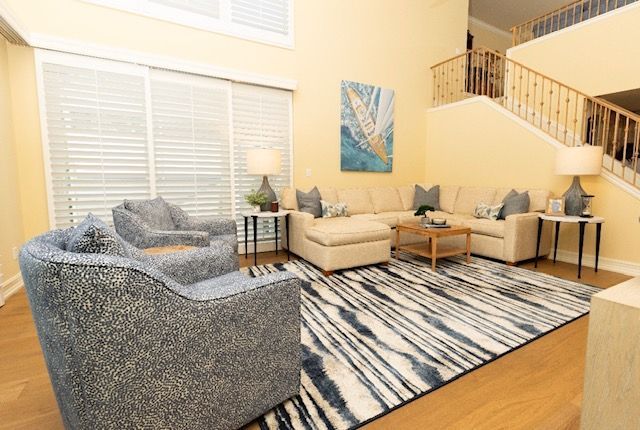 Living room with beige sectional, patterned rug, blue armchairs, and staircase.