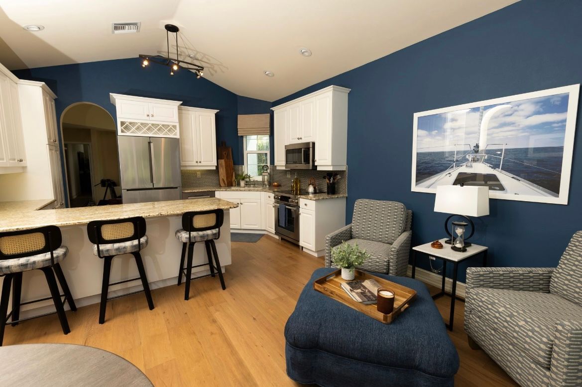 Open-concept kitchen and living room with blue walls, white cabinets, and wood floors. Seating and artwork.