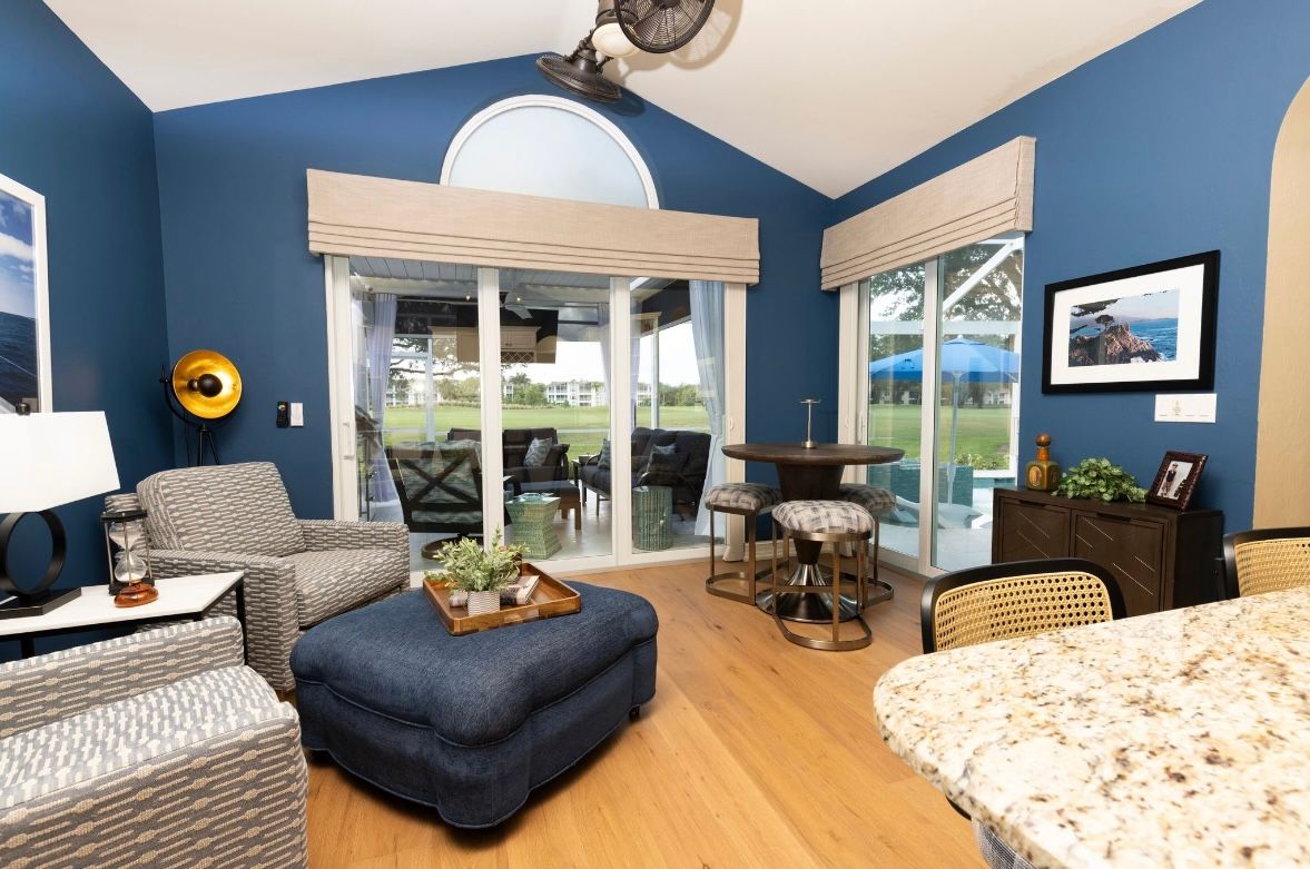 Blue-walled living area with patio view; chairs, ottoman, bar, sliding glass doors, and a ceiling fan.