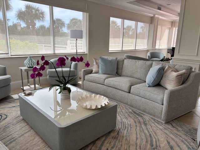 A light-filled living room with grey furniture, orchid, and coastal decor.