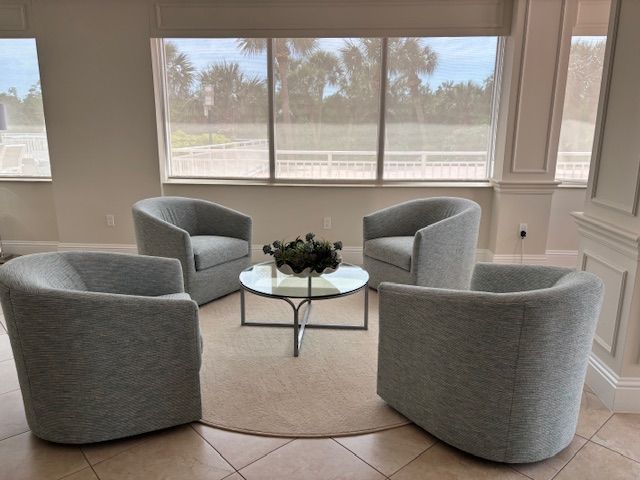 Four gray armchairs arranged around a glass-topped table in a well-lit room.