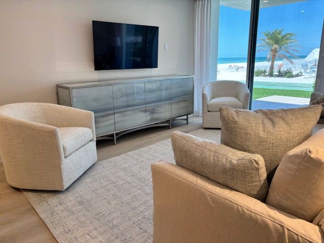 Living room with neutral decor and ocean view, featuring a TV, credenza, armchairs, and sofa on a rug.