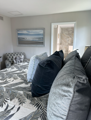 Bedroom with bed covered in black and white floral bedding and gray pillows, ocean art.