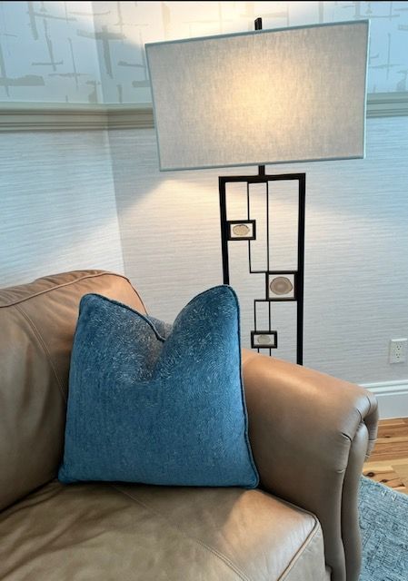 Blue pillow on a tan leather couch, with a black geometric lamp behind it.