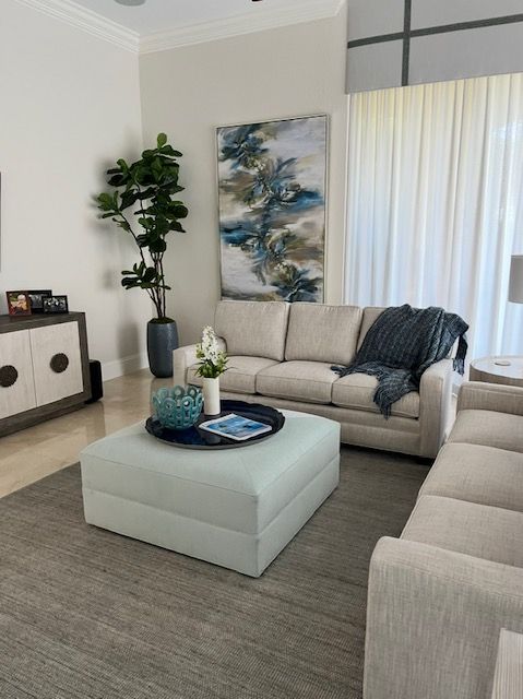 Living room with light-colored sofa, blue art, and large ottoman; neutral tones with plant and gray rug.