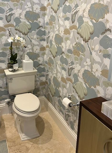 Powder room with floral wallpaper, white toilet, orchid, and a wooden cabinet.