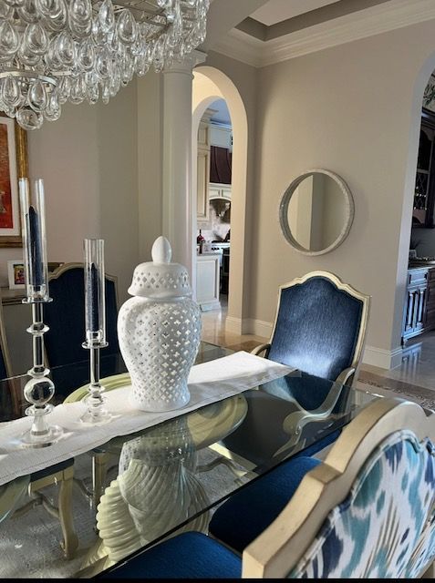 Dining room with a glass table, blue chairs, white decor, and a chandelier.