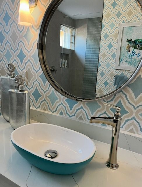 Bathroom with teal oval sink, patterned wall, and silver faucet.