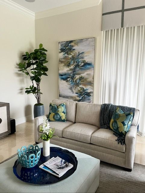 Living room with cream-colored sofa, blue art, large plant, and decorative tray on a blue ottoman.