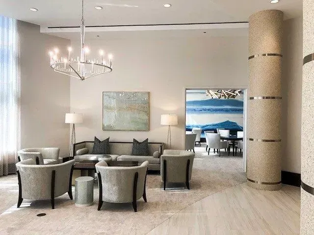 Lounge area with a sofa, chairs, artwork, and a chandelier. Neutral tones and a view into a dining space.