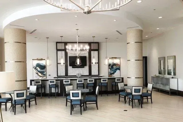Upscale bar/lounge with blue chairs, a bar, and pillars in a bright room with modern artwork.