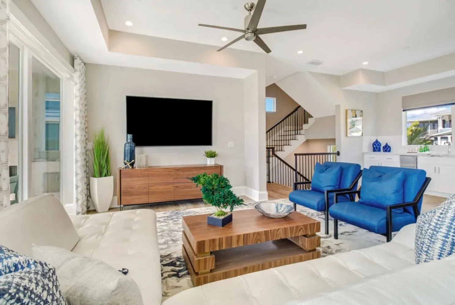 Bright living room with modern furniture, blue accents, and a staircase.