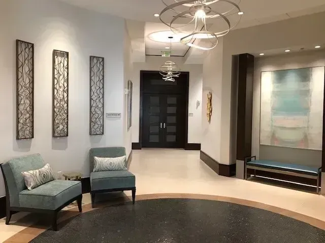 Lobby with teal chairs, artwork, and a bench; dark floor and walls; circular entry area.