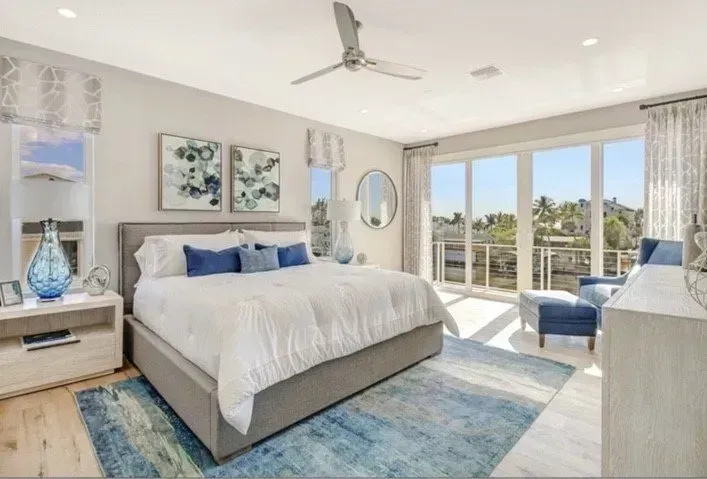 Bright bedroom with king bed, blue accents, large windows, and water view.