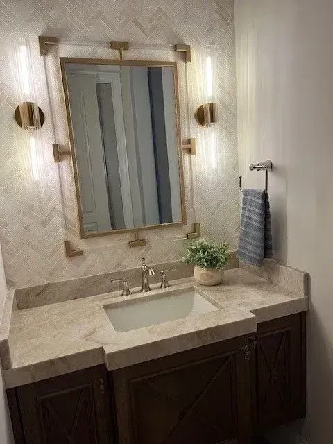 Bathroom vanity with rectangular mirror, gold accents, sconces, and stone countertop.