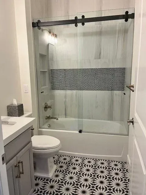 Bathroom with black and white patterned floor, white fixtures, and glass sliding shower door.
