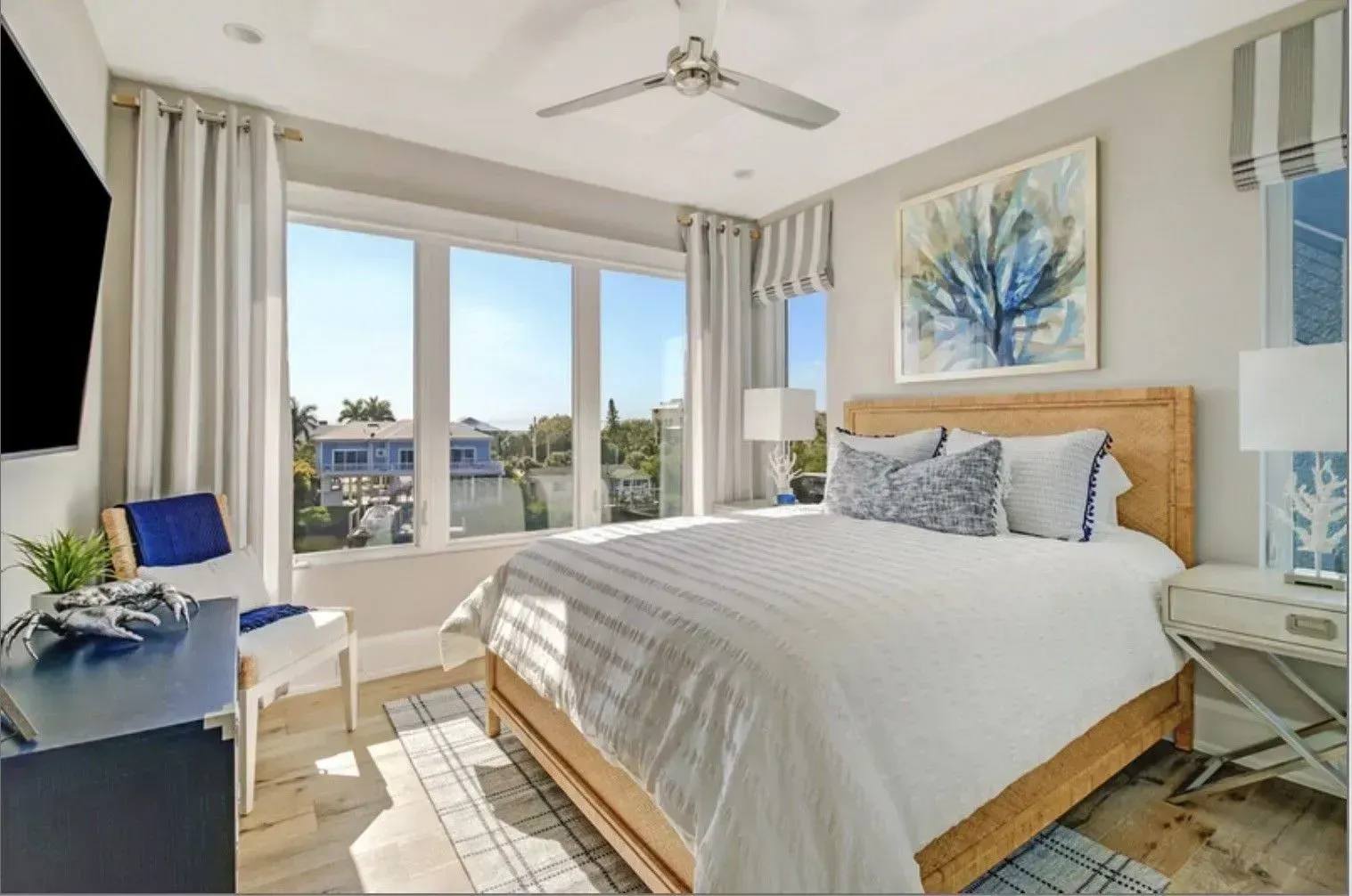 Bedroom with large window, white bed, blue accents, artwork, and water view.