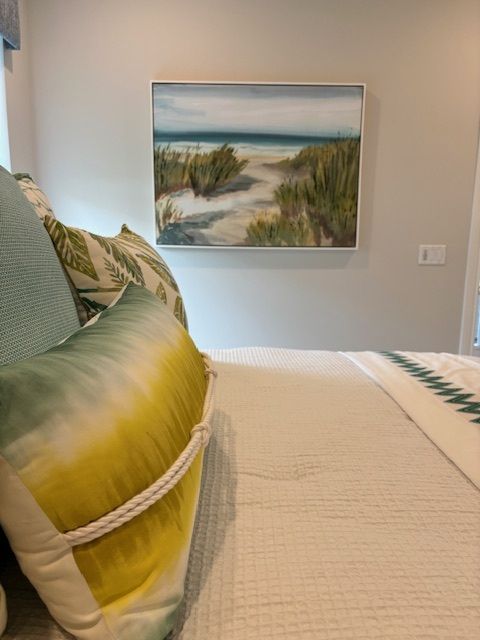 Bedroom with bed, pillows, beach painting, and neutral walls.