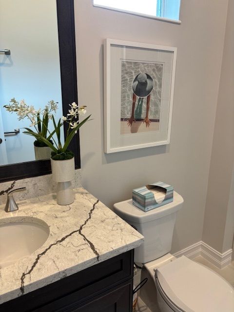 Cozy green armchair with a yellow pillow, by a painting and a weathered mirror. Neutral walls, light wood floor.