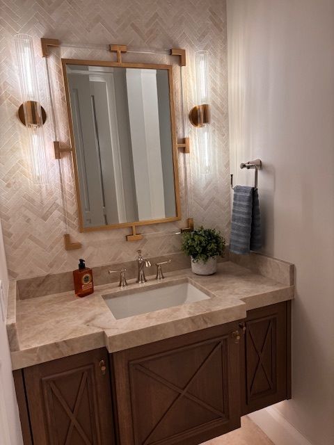 A powder room with a wooden vanity, ornate mirror, and sconces; a small plant sits on the counter.
